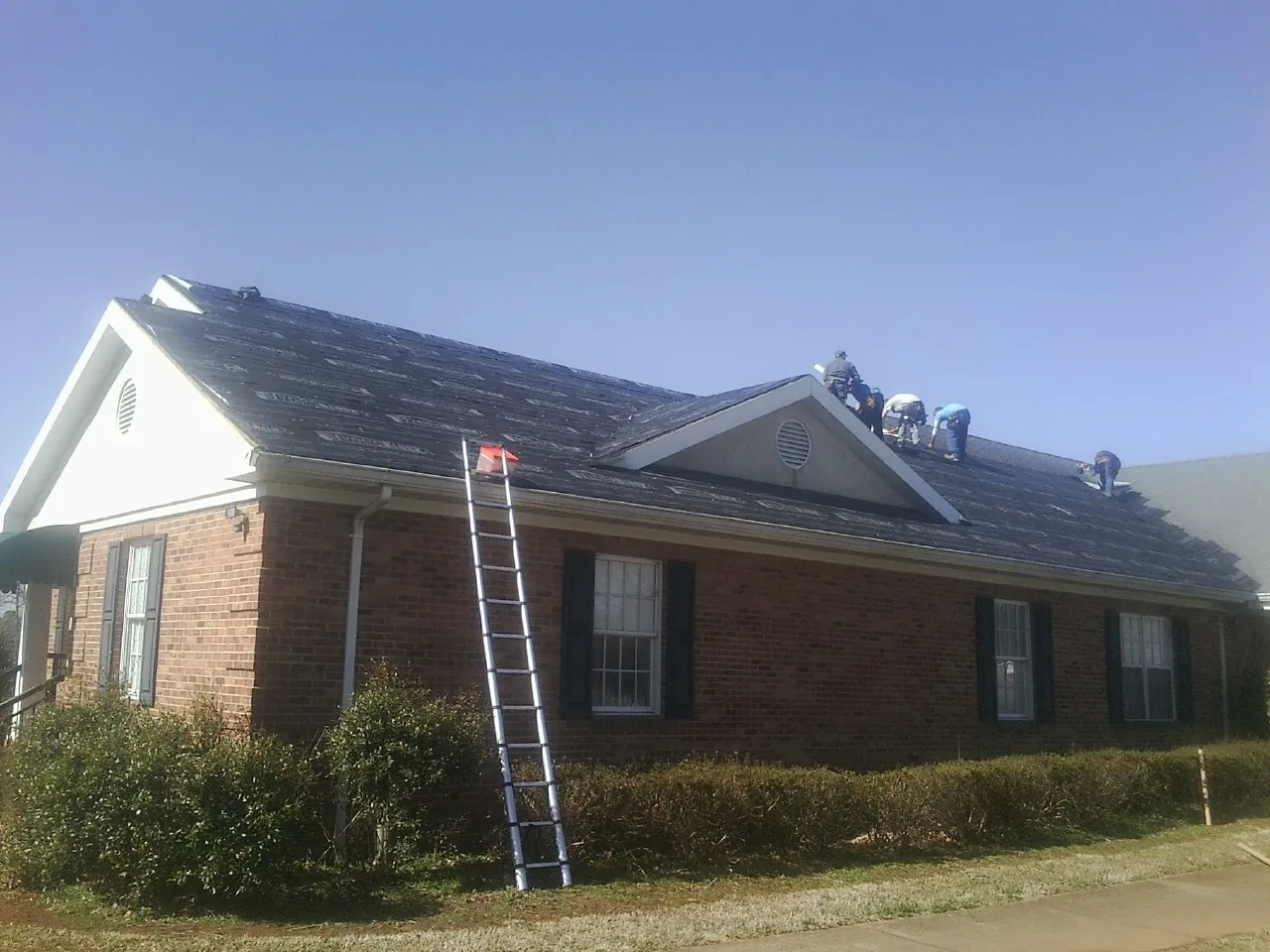Crew tearing shingles off a brick ranch roof with a ladder set — Emergency Roof Repair work by our crew in Newberg
