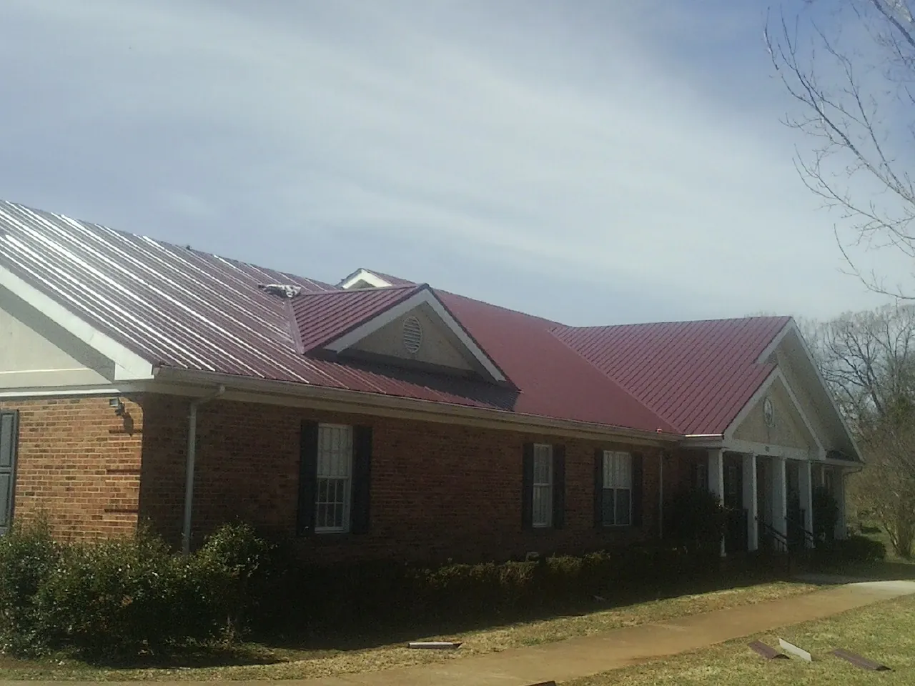 Red metal roof with gabled entries on a long brick building, from a Hail Damage Roof Repair job in Newberg