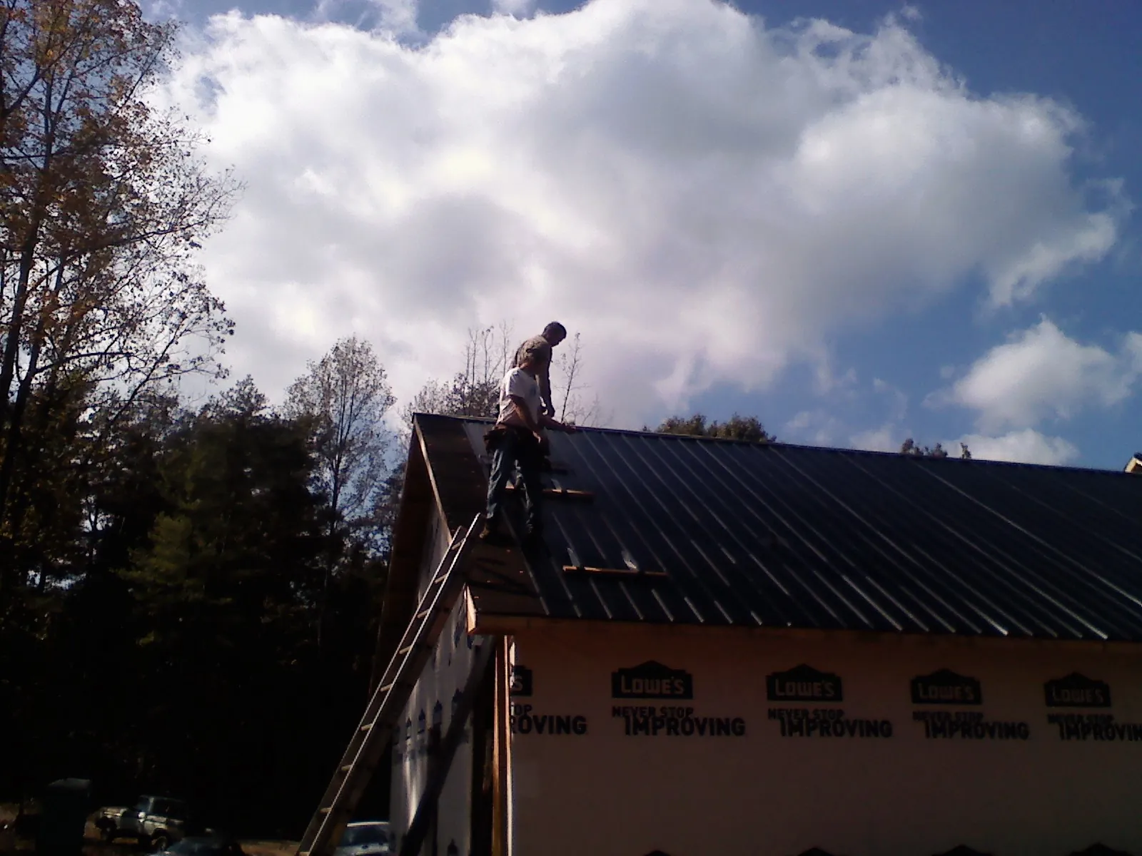 Roofer fastening dark metal panels high against a cloudy sky, from a Roof Inspection job in Newberg